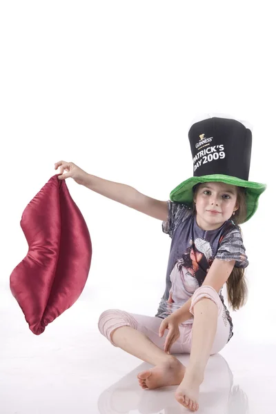 Dziewczynka siedzi na podłodze w czarnym kapeluszu, trzymając usta miękkie zabawki — Zdjęcie stockowe