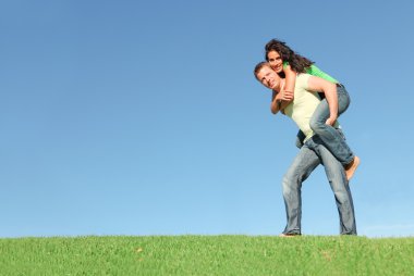 Happy smiling couple outside on grass giving piggy back clipart