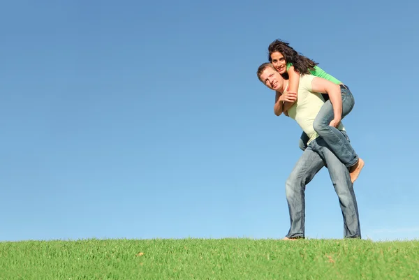 Glückliches lächelndes Paar draußen auf dem Gras gibt Huckepack zurück — Stockfoto