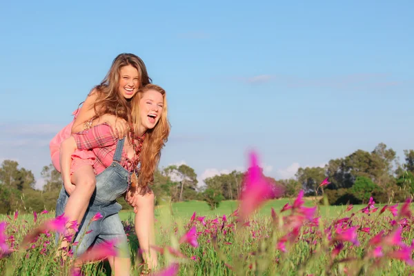 Glada leende våren eller sommaren piggy back tonåringar eller tonåringar — Stockfoto