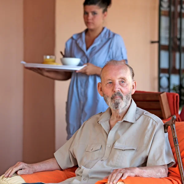 Senior med vårdare eller sjuksköterska föra måltid — Stockfoto