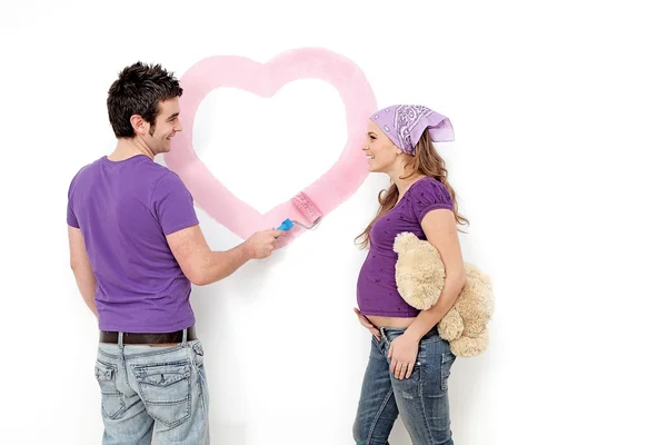 Junges Paar, Mann und schwangere Frau bemalen Kinderzimmer-Wand. — Stockfoto