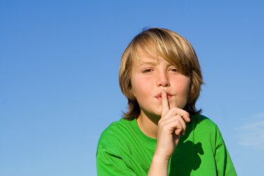 Child with finger to lips to ask for quiet or silence clipart