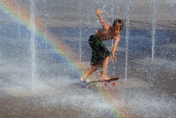 Kid cooling off playing on skateboard in fountain — Stock Photo, Image