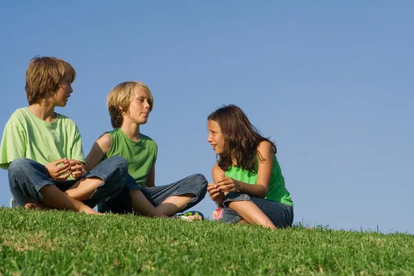 Bambini o bambini seduti fuori a chiacchierare sull'erba , — Foto Stock