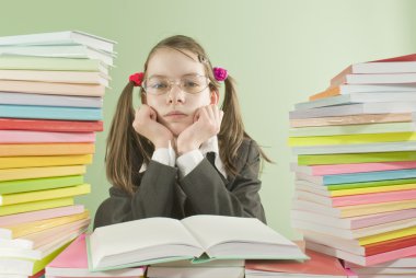 Bored school girl sitting at the table with stacks of books clipart