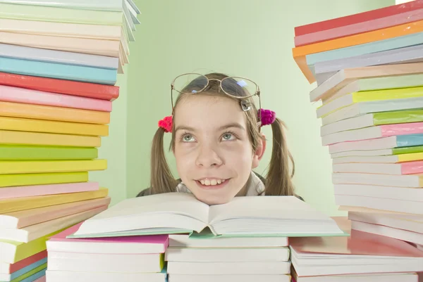 Escola menina sentada à mesa com pilhas de livros — Fotografia de Stock