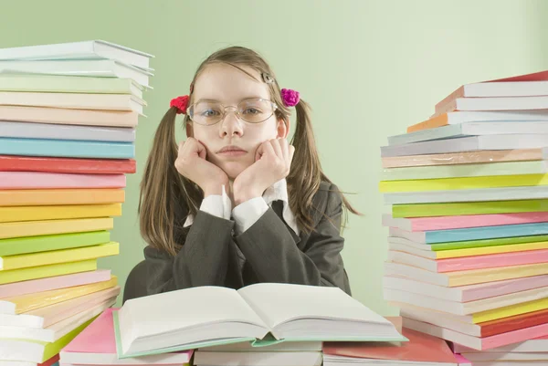 Verveeld school meisje zit aan de tafel met stapels van boeken — Stockfoto