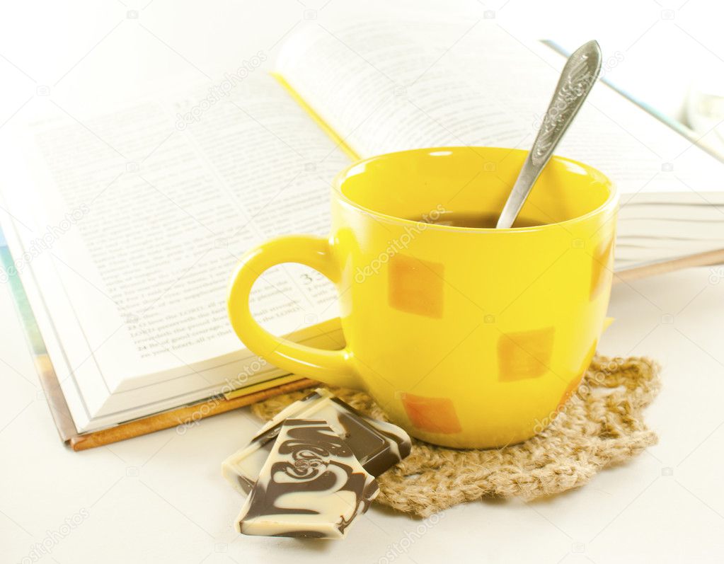 Yellow cup of tea with chocolate and book