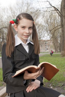 Teen girl with a book in a park clipart