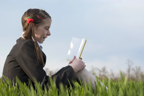 Dívka s knihou sedící v trávě — Stock fotografie