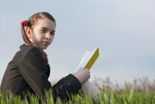 Dívka s knihou sedící v trávě Royalty Free Stock Fotografie