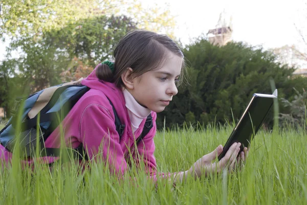 Девочка-подросток читает электрическую книгу, лежащую на траве — стоковое фото