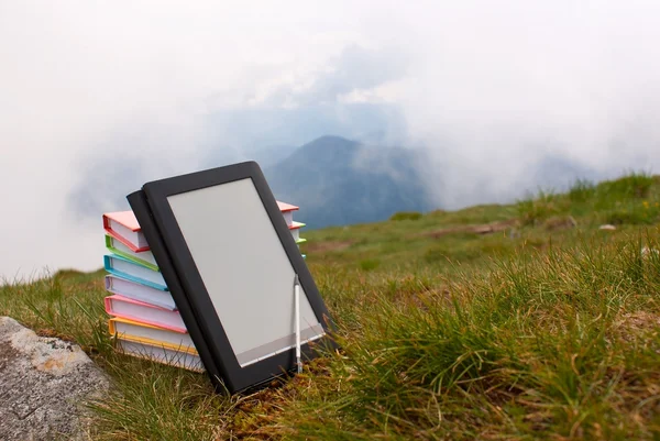 Stapel van kleurrijke boeken en elektronische boek lezer op het gras — Stockfoto