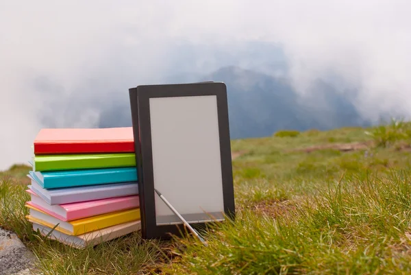Pila de libros coloridos y lector de libros electrónicos en la hierba — Foto de Stock