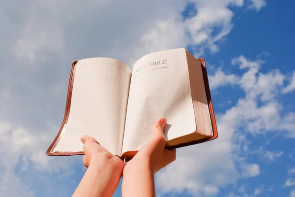 Ręce trzymać otwarte Biblii przeciw błękitne niebo — Zdjęcie stockowe