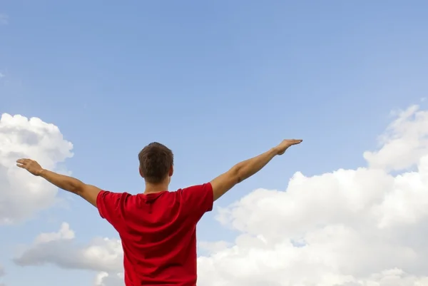 Young man staying with raised hands against blue sky — Stock Photo, Image
