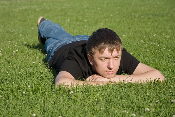 Sad young man lying on the grass in the park — Stock Photo, Image