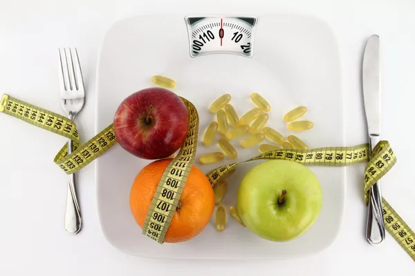 Frutas e vitaminas com fita métrica em um prato como balança de peso — Fotografia de Stock