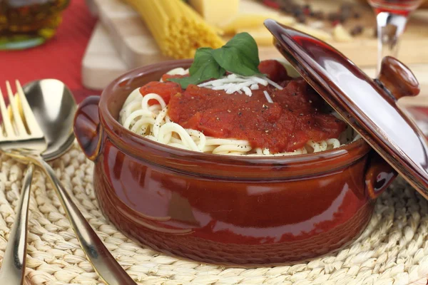 Makaron spaghetti z sosem pomidorowym, serem i bazylią w glinianym garnku — Zdjęcie stockowe