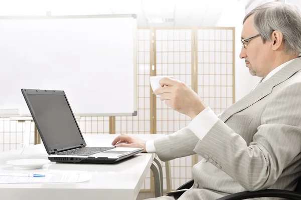 Retrato de un hombre de negocios mayor con una computadora y una taza . — Foto de Stock