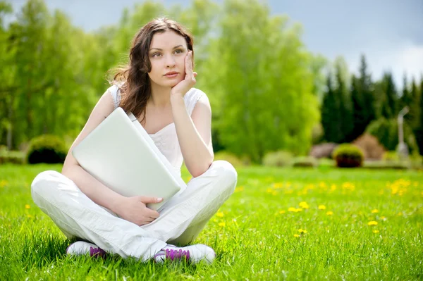 Mladá žena s notebookem sedí na zelené trávě — Stock fotografie