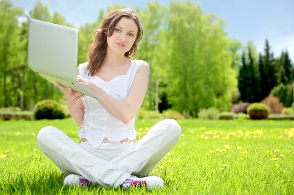Молода жінка з ноутбуком сидить на зеленій траві — стокове фото