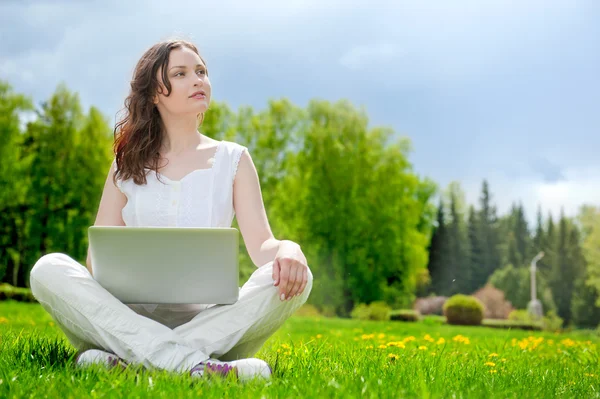 Молода жінка з ноутбуком сидить на зеленій траві — стокове фото