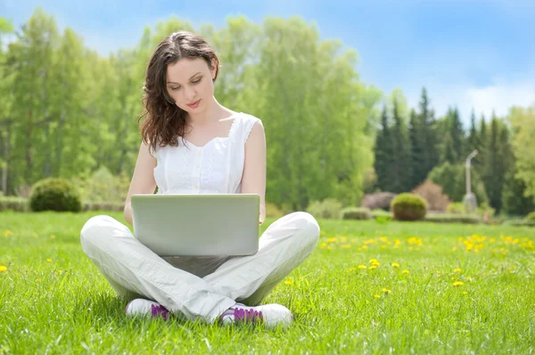 Νεαρή γυναίκα με φορητό υπολογιστή κάθεται στο πράσινο γρασίδι — Φωτογραφία Αρχείου
