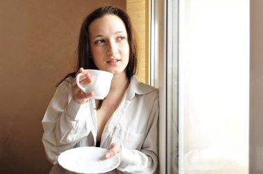 Portrait of cosy young girl standing near a window at home clipart