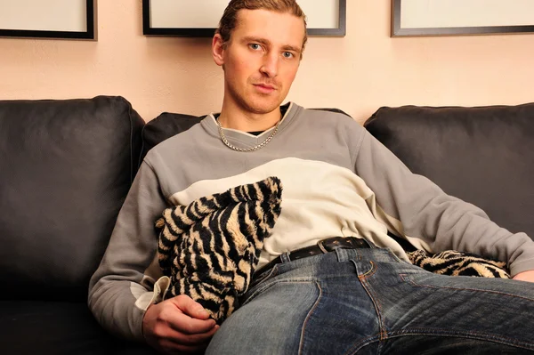 Happy young man sitting on sofa at home — Stock Photo, Image