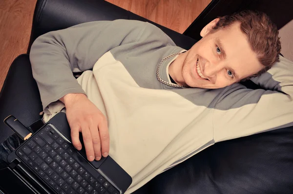 Evde bir kanepede oturan mutlu bir genç adam — Stok fotoğraf