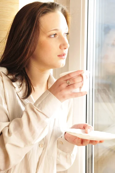 Портрет уютной молодой девушки, стоящей у окна дома — стоковое фото