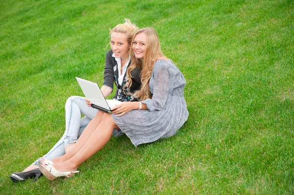 Retrato de dos mujeres sonrientes usando el ordenador portátil en un prado verde en — Foto de Stock