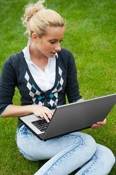 Jeune femme avec ordinateur portable assis sur l'herbe verte et regardant à th — Photo