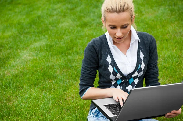 Yeşil çimenlerin üzerinde oturan ve th için seyir laptop ile genç kadın — Stok fotoğraf