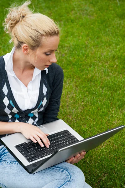 Mujer joven con portátil sentado en la hierba verde y mirando a th —  Fotos de Stock