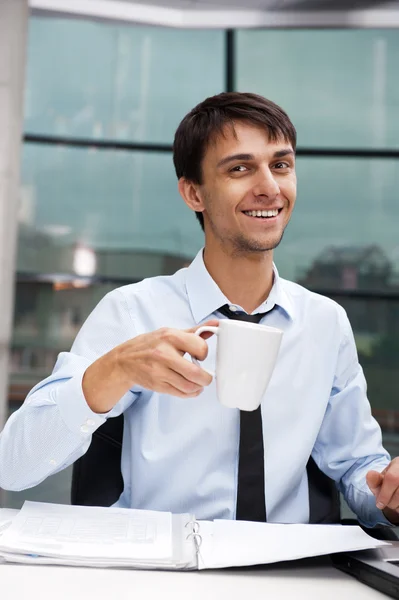 Νέος επιχειρηματίας, έχοντας ένα διάλειμμα για καφέ το πρωί, κάθεται στο γραφείο — Φωτογραφία Αρχείου