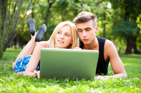 Retrato de jovem casal ao ar livre descansando na grama verde e usin — Fotografia de Stock