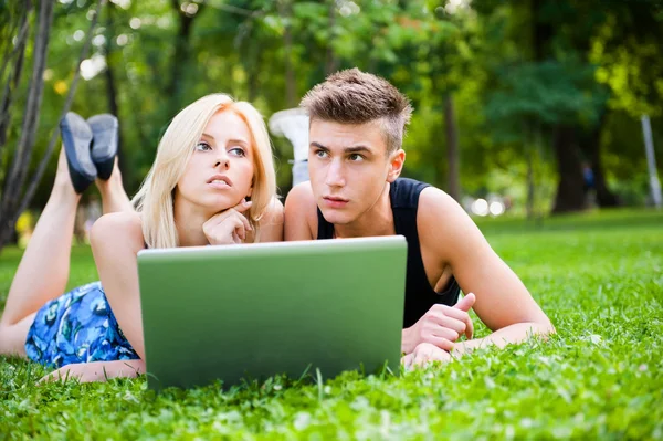Retrato de jovem casal ao ar livre descansando na grama verde e usin — Fotografia de Stock