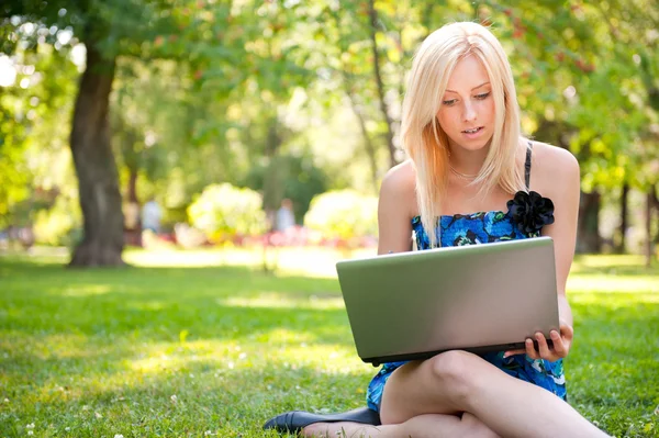 Hermosa mujer estudiante con un ordenador portátil sentado en la hierba verde en —  Fotos de Stock