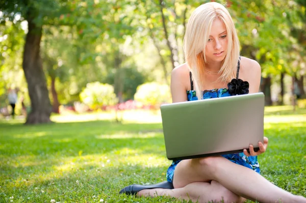 Vacker student kvinna med en laptop sitter på grönt gräs på — Stockfoto