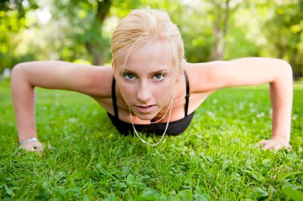 Pełna długość młoda kobieta robi pompki na zielonej trawie w srokaty — Zdjęcie stockowe