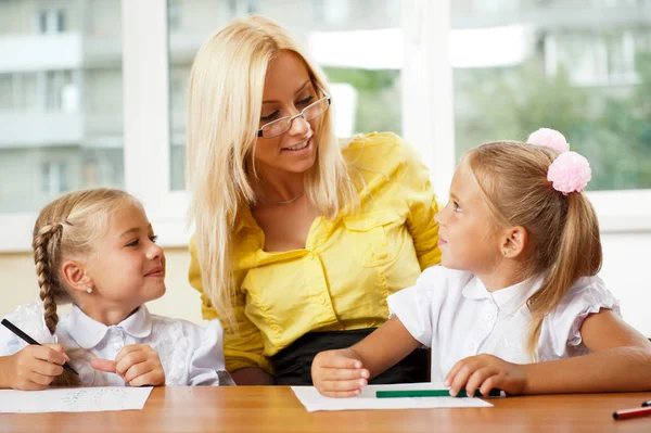 Teacher helps to little girls to make an exercises in classroom — Stock Photo, Image