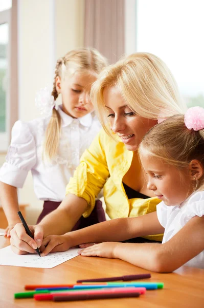 Giovane bella insegnante aiutare i suoi piccoli studenti in classe — Foto Stock