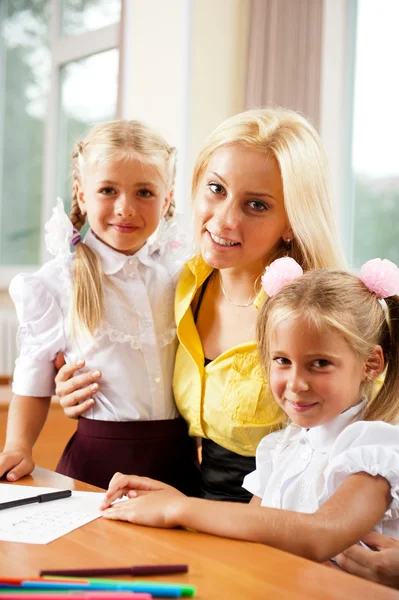 Молодая красивая учительница помогает своим маленьким ученикам в классе — стоковое фото