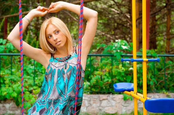 Portrait of pretty young woman swinging on playground at park an — Stock Photo, Image