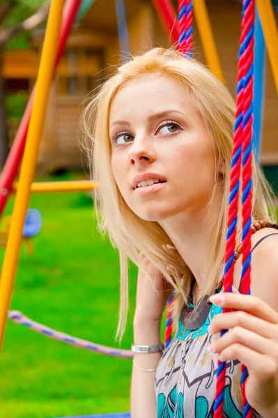 Portrait of pretty young woman swinging on playground at park an — Stock Photo, Image