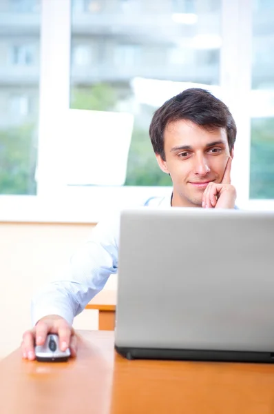 Ένας νεαρός άνδρας κάθεται μπροστά από ένα φορητό υπολογιστή στο γραφείο του — Φωτογραφία Αρχείου