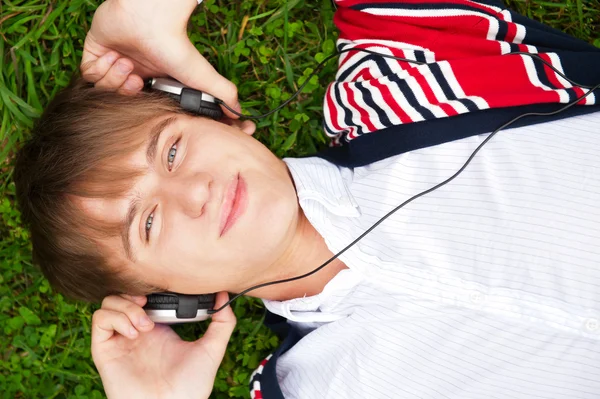 Estudiante fuera acostado en la hierba y escuchando la escuela de música. Fotógrafo — Foto de Stock